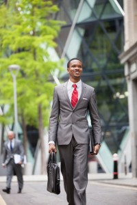 Happy African American businessman with bag walking on street