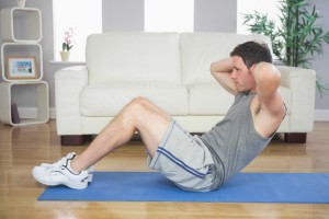Fit handsome man doing sit ups in bright living room