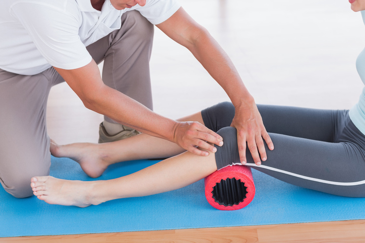 Trainer working with woman on exercise mat in fitness studio